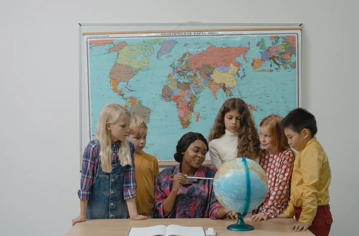 Teacher and students examining a globe in front of a classroom world map